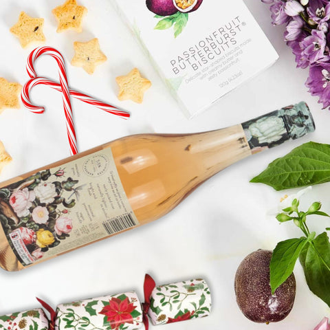 Bottle of Rosé wine with Christmas-themed packaging, surrounded by cookies, a candy cane, and decorative items on a white surface.