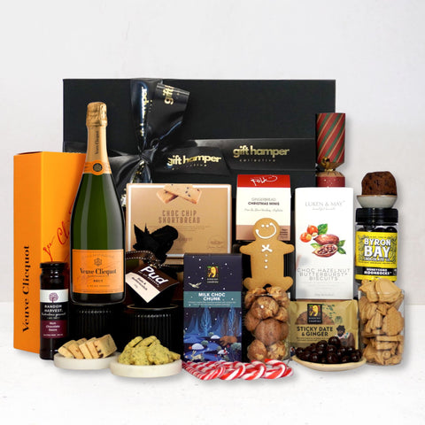 Gift hamper with various items including a bottle of Veuve champagne, cookies, and a box of chocolates on a white background.